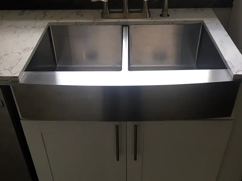New stainless farmhouse sink with a pull-down faucet in a white kitchen