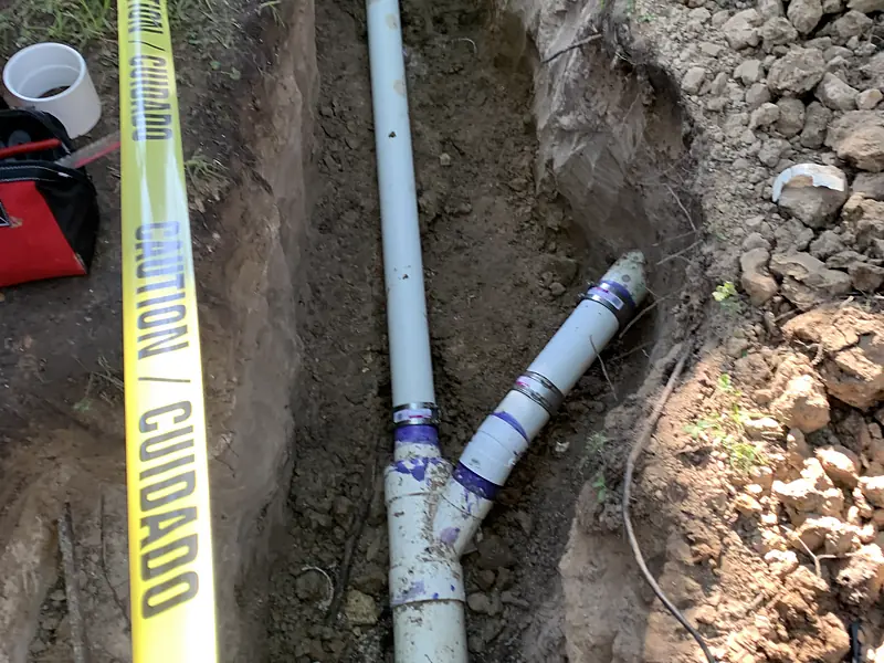New PVC sewer line laid in an open trench marked with caution tape