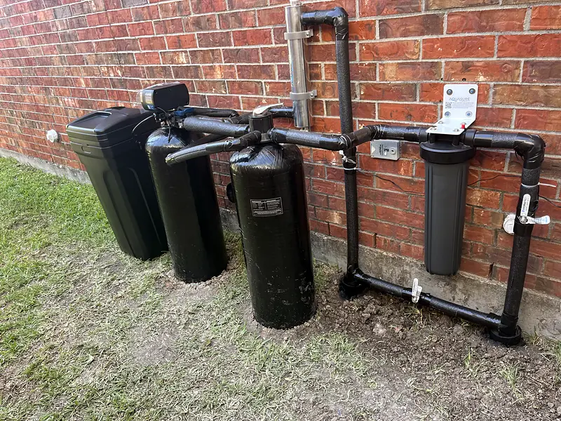 Outdoor water softener and filtration tanks beside a brick house