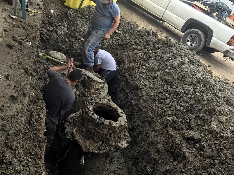Crew lowering a yellow tank into an excavated pit beside a truck