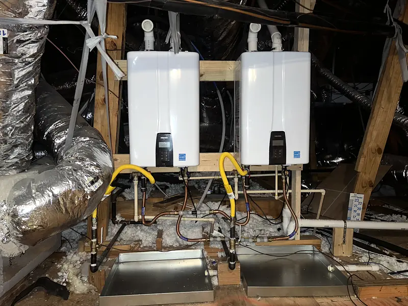 Two tankless water heaters mounted in an attic with drain pans