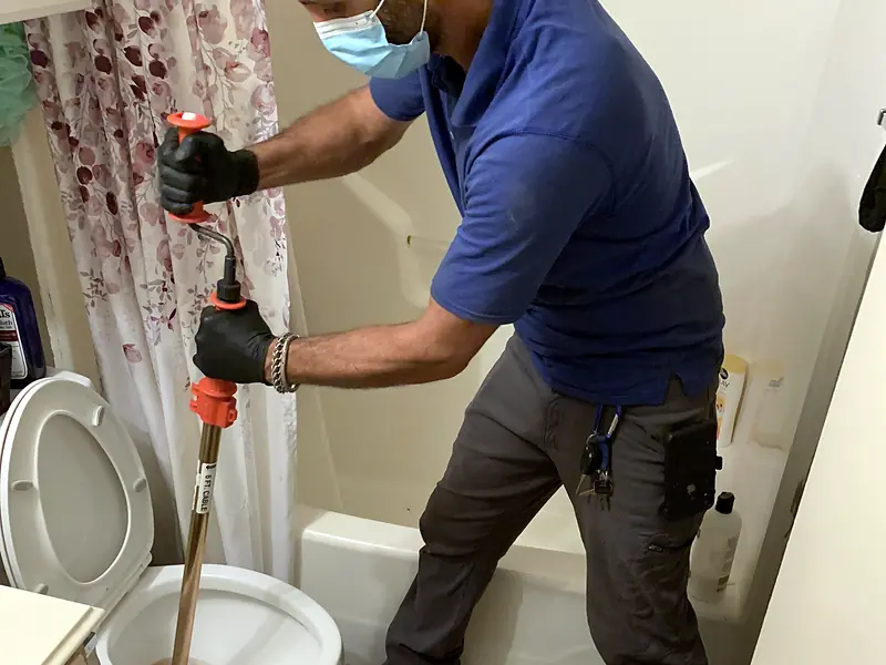Royal Flush Affordable Plumbing plumber clearing a toilet with a closet auger in a home bathroom