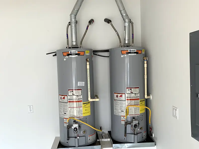 Two new gas tank water heaters installed side by side in a garage