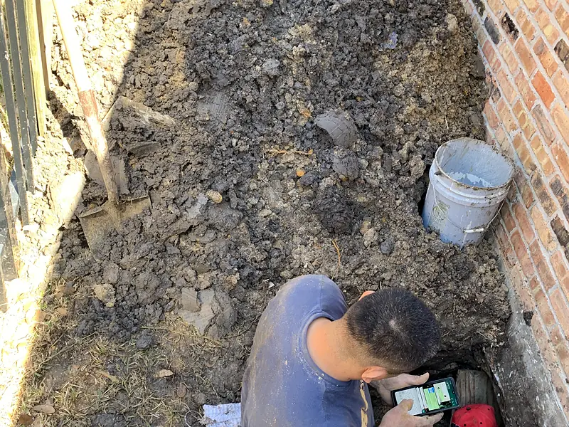 Two plumbers working in a dug-out area beneath a brick foundation