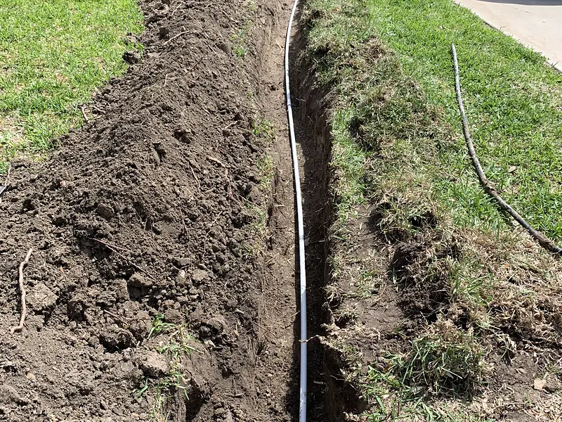 Narrow trench across a lawn with a new water line and the service van behind