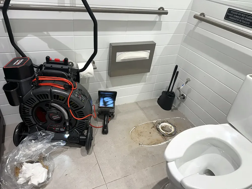 Drain camera reel and monitor set up on the floor of a commercial restroom with the toilet flange exposed