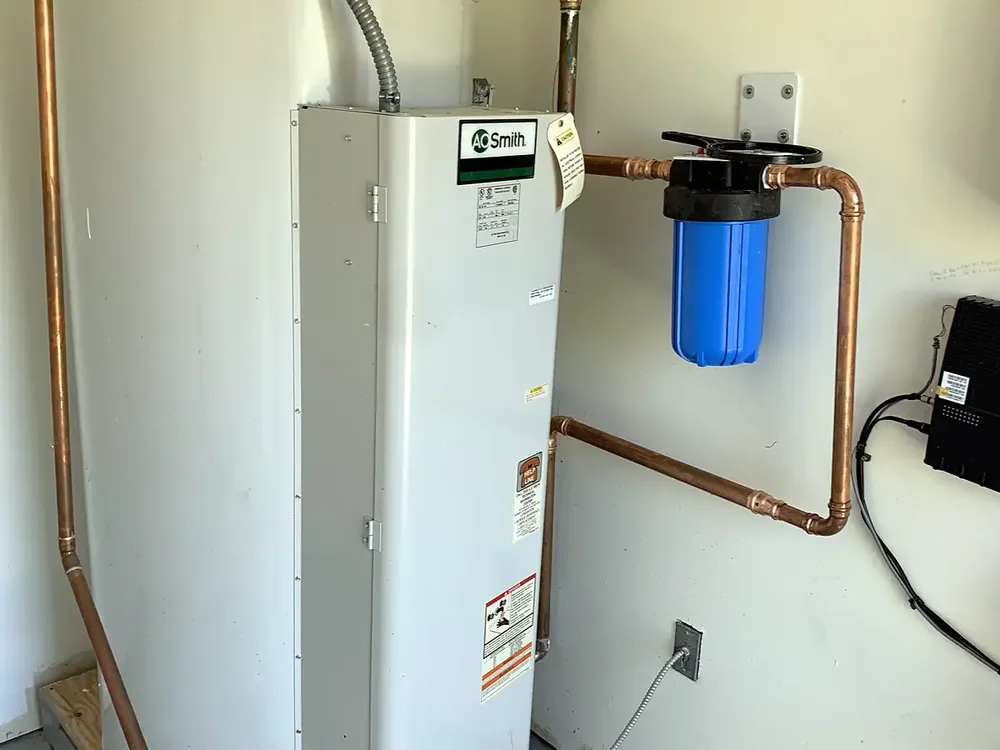 Filter housing with a blue canister plumbed into the copper supply line next to an electric water heater