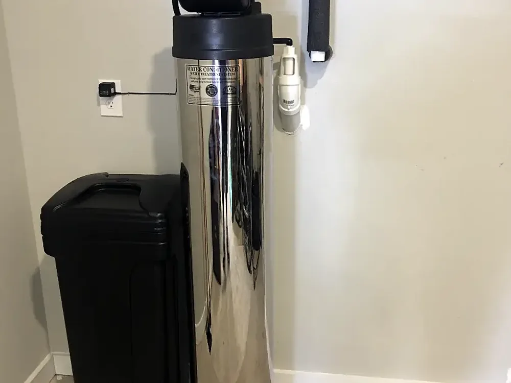 Stainless steel water conditioner with a black brine tank beside it, plugged in and plumbed in