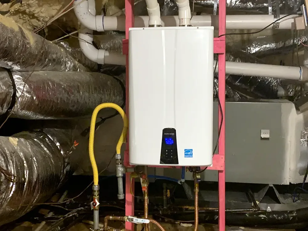 Wall-mounted tankless water heater in an attic with a yellow flexible gas connector and shutoff valve